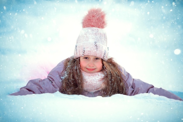 Foto ein mädchen im grundschulalter liegt im schnee und lächelt