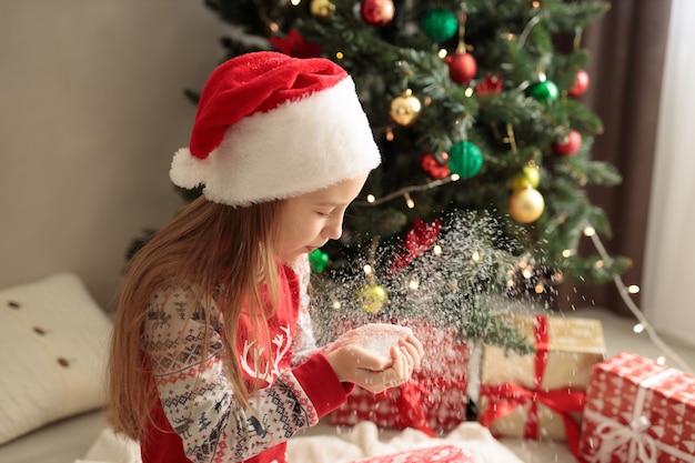 Ein Mädchen im Neujahrspyjama Ein Mädchen bläst Schnee von ihren Handflächen