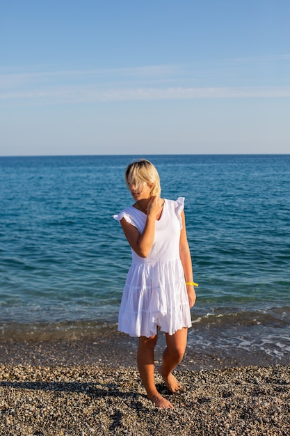 Ein Mädchen im weißen Kleid, das am Meer spazieren geht