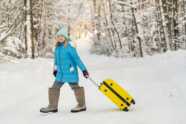 Ein Mädchen im Winter in Filzstiefeln geht mit einem Koffer an einem frostigen Schneetag
