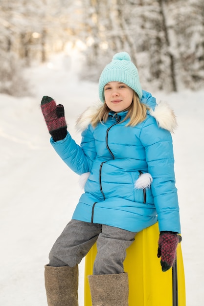 Ein Mädchen im Winter in Filzstiefeln sitzt an einem frostigen Schneetag auf einem Koffer.