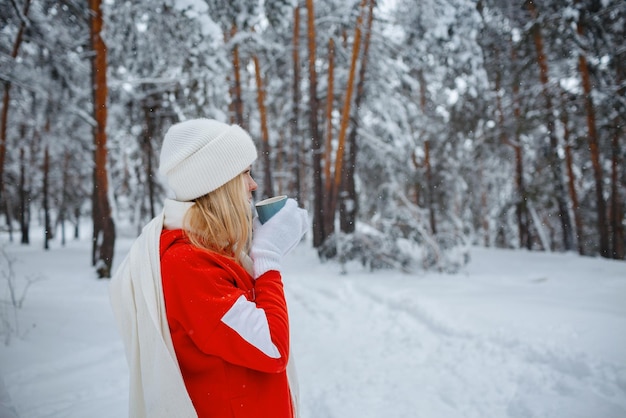 Ein Mädchen im Winterwald, eine Blondine in roten Kleidern, ein lustiger Spaziergang in der Natur