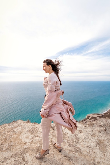 ein Mädchen in Beige geht auf einem Felsen vor dem Hintergrund des Meeres