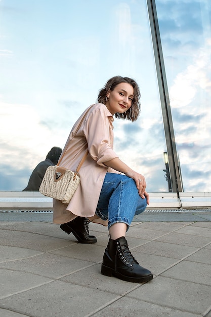 Ein Mädchen in Blue Jeans und einem beigen Hemd gegen eine Glaswand. Porträt einer jungen Frau. Urbaner Stil.