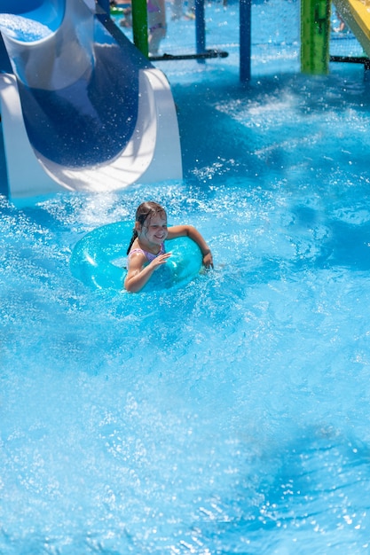 Ein Mädchen in einem aufblasbaren Kreis rutscht eine Wasserrutsche in den Pool und schickt Wasserspritzer in...
