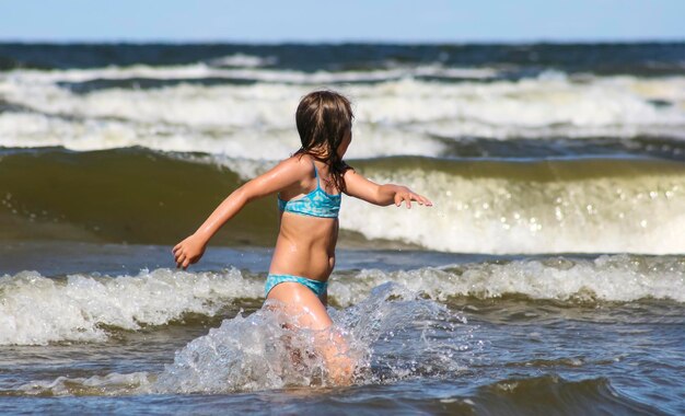 Ein Mädchen in einem Badeanzug am Meer läuft an einem warmen, sonnigen Sommertag entlang der großen Wellen