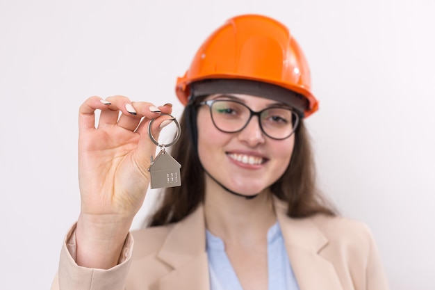 Ein Mädchen in einem Bauhelm hält ein Haus. Grundstücksmakler auf weißem Hintergrund.