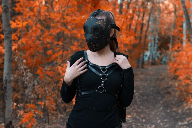 Ein Mädchen in einem BDSM-Kostüm und einer schwarzen Maske in einem roten Wald. Eine Idee für Halloween.