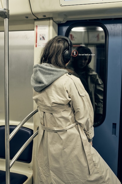 Ein Mädchen in einem beigen Trenchcoat fährt in einem U-Bahn-Wagen.