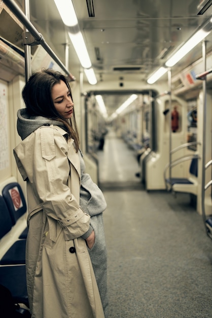 Ein Mädchen in einem beigen Trenchcoat fährt in einem U-Bahn-Wagen.