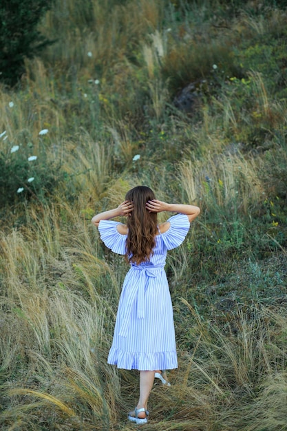 Ein Mädchen in einem blauen Kleid in der Nähe des Waldes in Pflanzen bei Sonnenuntergang