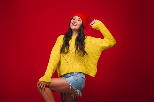 Ein Mädchen in einem gelben Pullover und einem Hut auf einem roten Hintergrund verzieht das Gesicht