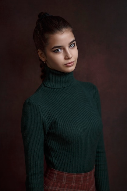 Ein Mädchen in einem grünen Pullover und Rock auf einem dunklen Hintergrund