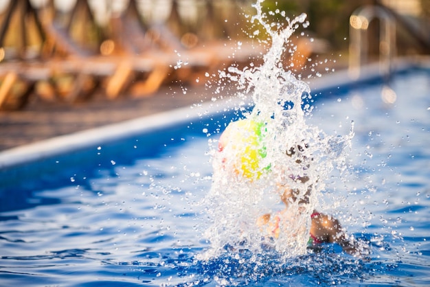 Ein Mädchen in einem hellen Badeanzug schwimmt an einem Sommerabend mit einem aufblasbaren Ball in einem Pool mit klarem Wasser
