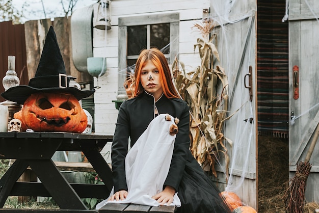 Foto ein mädchen in einem hexenkostüm mit einem hund in einem geisterkostüm hat spaß auf der veranda eines hauses, das dekoriert ist, um eine halloween-party zu feiern