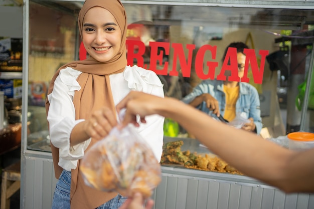 Ein Mädchen in einem Hijab, das frittierte Lebensmittel verkauft, gibt einem Käufer eine frittierte Bestellung