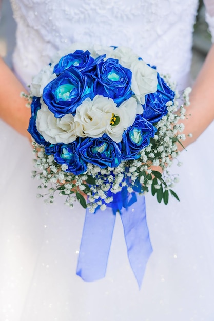 Ein Mädchen in einem Hochzeitskleid hält einen Blumenstrauß aus weißen und blauen Rosen in der Nähe