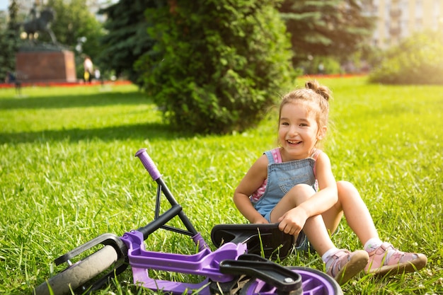 Ein Mädchen in einem Jeansoverall fährt im Sommer ein lila Laufrad in einem grünen Park