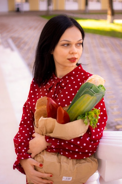 Ein Mädchen in einem Kleid geht die Straße entlang und hält eine Papiertüte mit Lebensmitteln in der Hand.