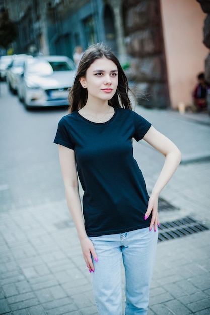 Ein Mädchen in einem leeren schwarzen T-Shirt und Jeans steht auf dem Straßenmodell für eine T-Shirt-Druckerei