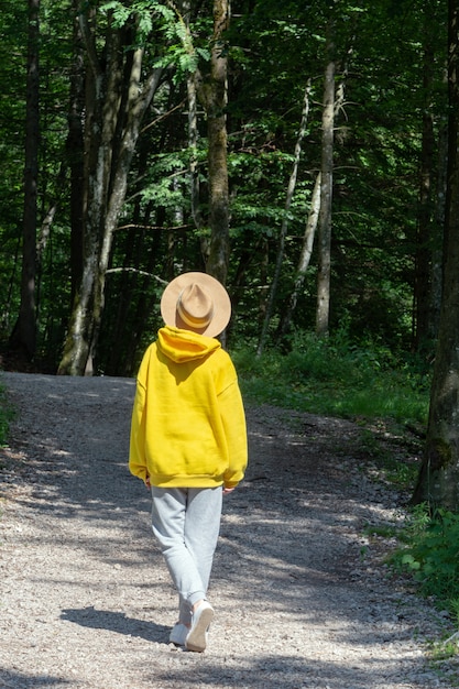 Ein Mädchen in einem leuchtend gelben Kapuzenpulli mit Hut geht einen Weg im Wald entlang.