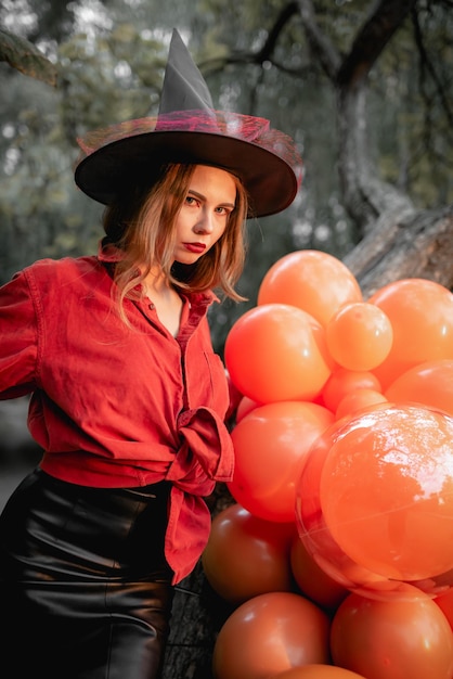 Ein Mädchen in einem orangefarbenen Hemd, einem schwarzen Rock und einem Hexenhut auf einem Hintergrund von Ballons Halloween-Party-Kunstdesign