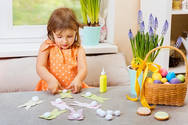 Ein Mädchen in einem orangefarbenen Kleid bastelt Osterhasen aus Papier für eine festliche Heimdekoration