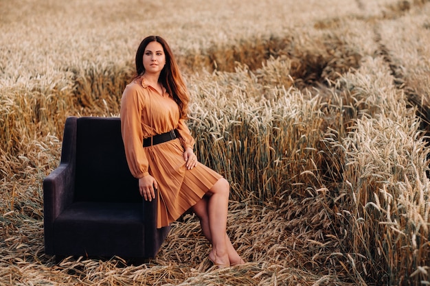 Ein Mädchen in einem orangefarbenen Kleid sitzt abends auf einem Stuhl in einem Weizenfeld