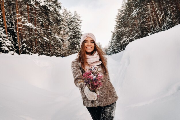 Ein Mädchen in einem Pullover im Winter mit einem Blumenstrauß in den Händen steht zwischen großen Schneeverwehungen.