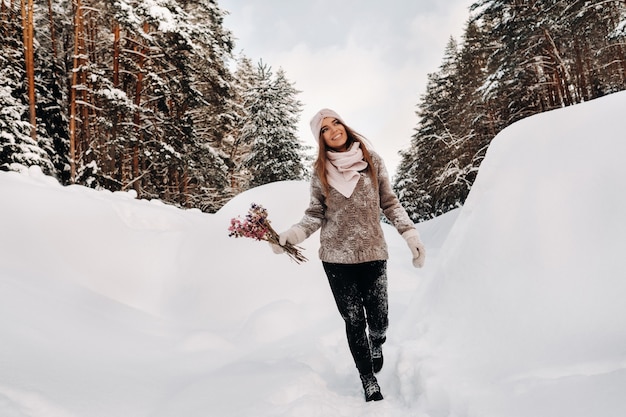 Ein Mädchen in einem Pullover im Winter mit einem Blumenstrauß in den Händen steht zwischen großen Schneeverwehungen.