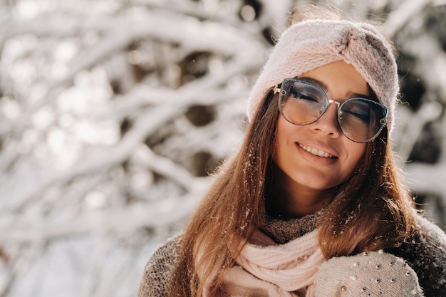 Ein Mädchen in einem Pullover und einer Brille im Winter in einem verschneiten Wald.