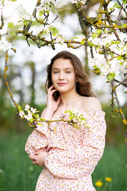 Ein Mädchen in einem rosa Kleid steht neben einem weißen Baum mit Blumen, schaut in die Kamera und lächelt