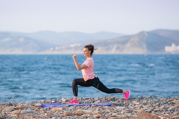 ein Mädchen in einem rosa T-Shirt und schwarzen Leggings macht Sport am Meer