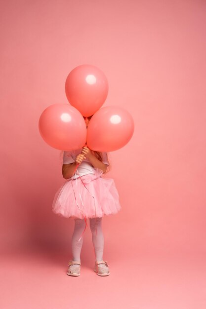 Ein Mädchen in einem rosa Tutu hält einen Haufen rosa Luftballons vor einem rosa Hintergrund