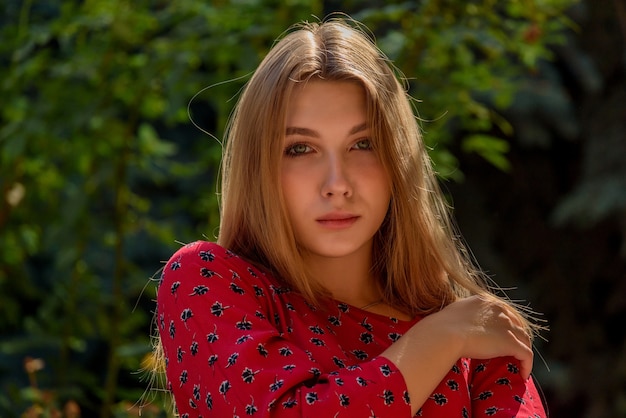 Ein Mädchen in einem roten Kleid mit langen Haaren auf grünem Hintergrund im Sommer. schönes Mädchen in der Natur