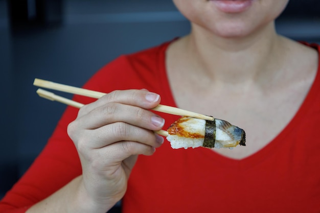 Ein Mädchen in einem roten Pullover hält Sushi mit Meeraal mit Essstäbchen Meeresfrüchte