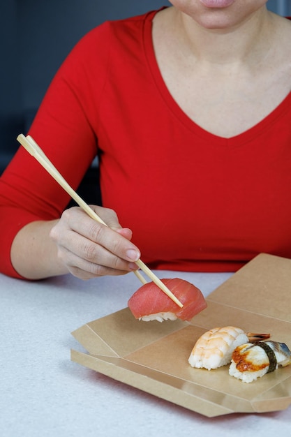 Ein Mädchen in einem roten Pullover hält Thunfisch-Sushi mit Essstäbchen Meeresfrüchte