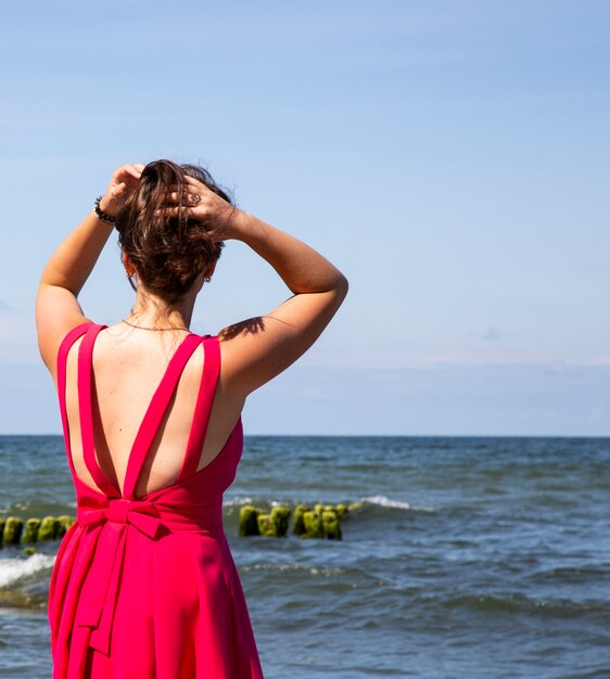 Ein Mädchen in einem scharlachroten Kleid am Meer. Wind, Wellen, einsamer Strand. Ein Urlaub im Süden