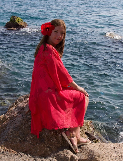 Ein Mädchen in einem scharlachroten Kleid am Meer. Wind, Wellen, einsamer Strand. Ein Urlaub im Süden