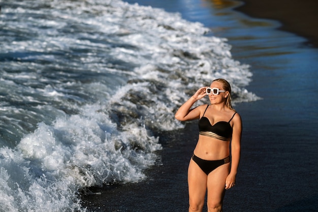 Ein Mädchen in einem schwarzen Badeanzug geht am Strand spazieren.