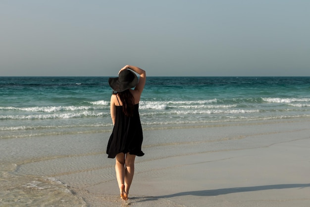 Ein Mädchen in einem schwarzen Hut und Kleid steht auf dem Hintergrund des Meeres