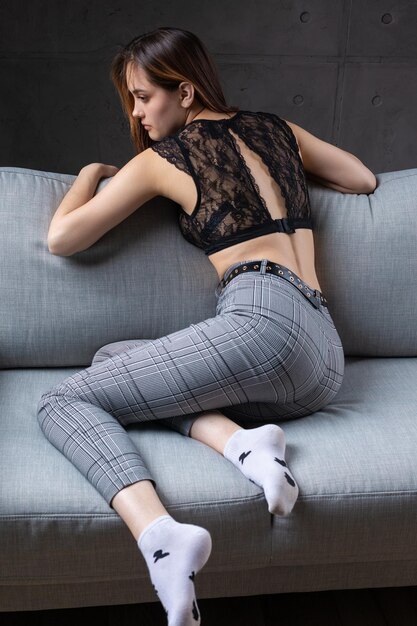 Ein Mädchen in einem schwarzen Spitzentop posiert auf einem grauen Sofa im Studio