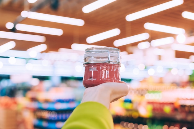 Ein Mädchen in einem Supermarkt hält ein Glas mit Honig in der Hand. vor dem Hintergrund von Lampen.