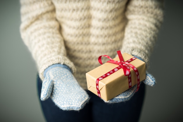 Foto ein mädchen in einem warmen strickpullover und fäustlingen hält ein weihnachtsgeschenk.