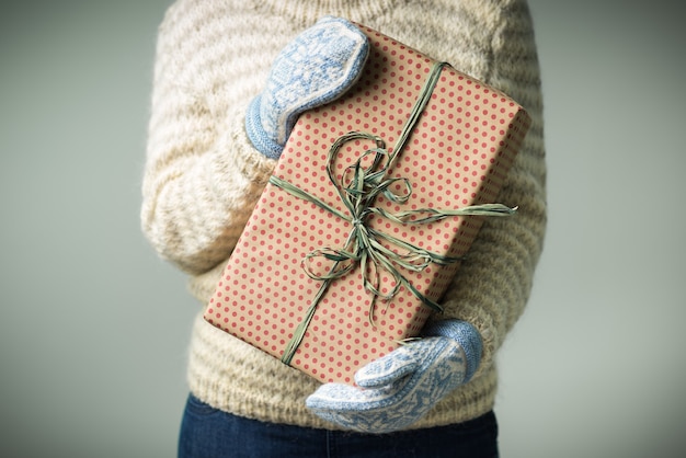 Ein Mädchen in einem warmen Strickpullover und Fäustlingen hält ein Weihnachtsgeschenk.