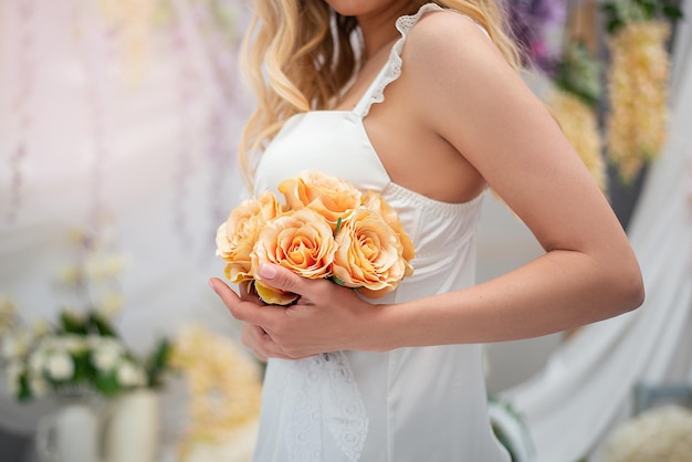 Ein Mädchen in einem weißen Bodysuit und einem sexy Frisiermantel mit einem Strauß Rosen, großen Händen, Romantik und Dekor