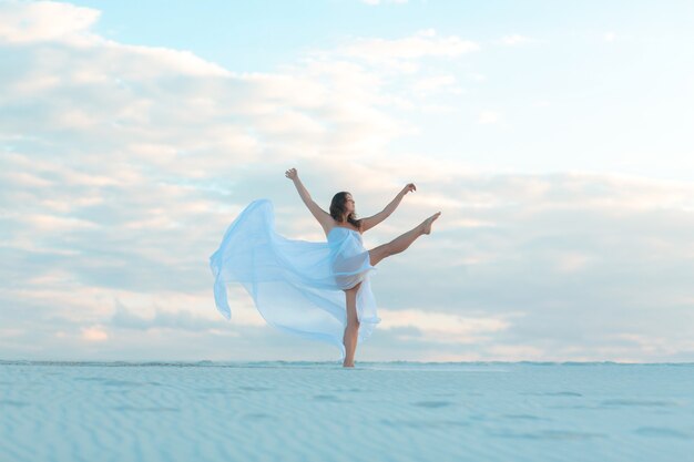 Ein Mädchen in einem weißen Kleid der Fliege tanzt und posiert in der Sandwüste bei Sonnenuntergang.