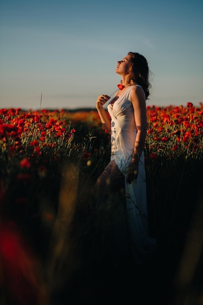 Ein Mädchen in einem weißen Kleid geht bei Sonnenuntergang durch ein Feld mit Mohnblumen