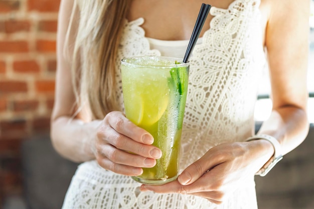 Ein Mädchen in einem weißen Kleid hält eine kalte Limonade in einem Glasglas in der Hand