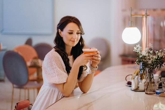 Ein Mädchen in einem weißen Kleid sitzt an der Bar in einem Café und trinkt einen Cocktail